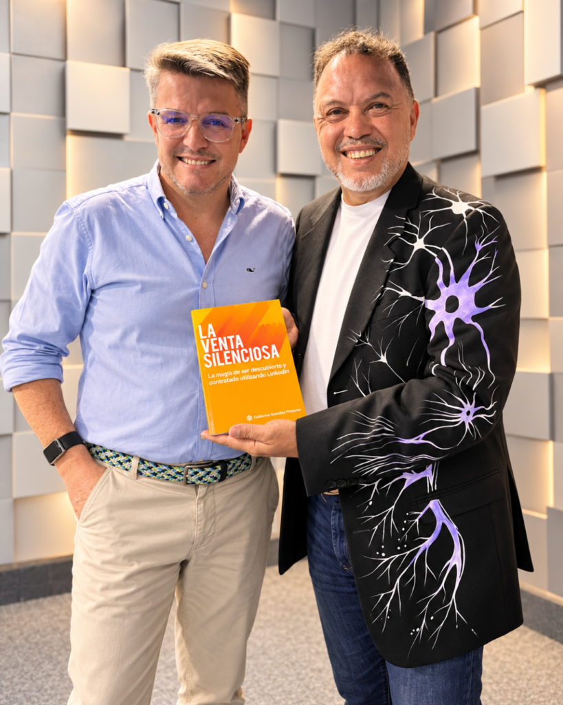 Guillermo González Pimiento hace entrega de un ejemplar de su libro La Venta Silenciosa a Carlos DeMente posan sonriendo mientras sostienen el libro impreso color naranja. Documentado por la Revista Club PRO.